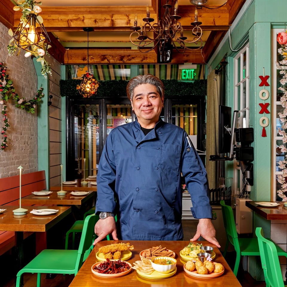 Chef in blue uniform stands behind a table with various Thai appetizers at Jai Dee Restaurant.