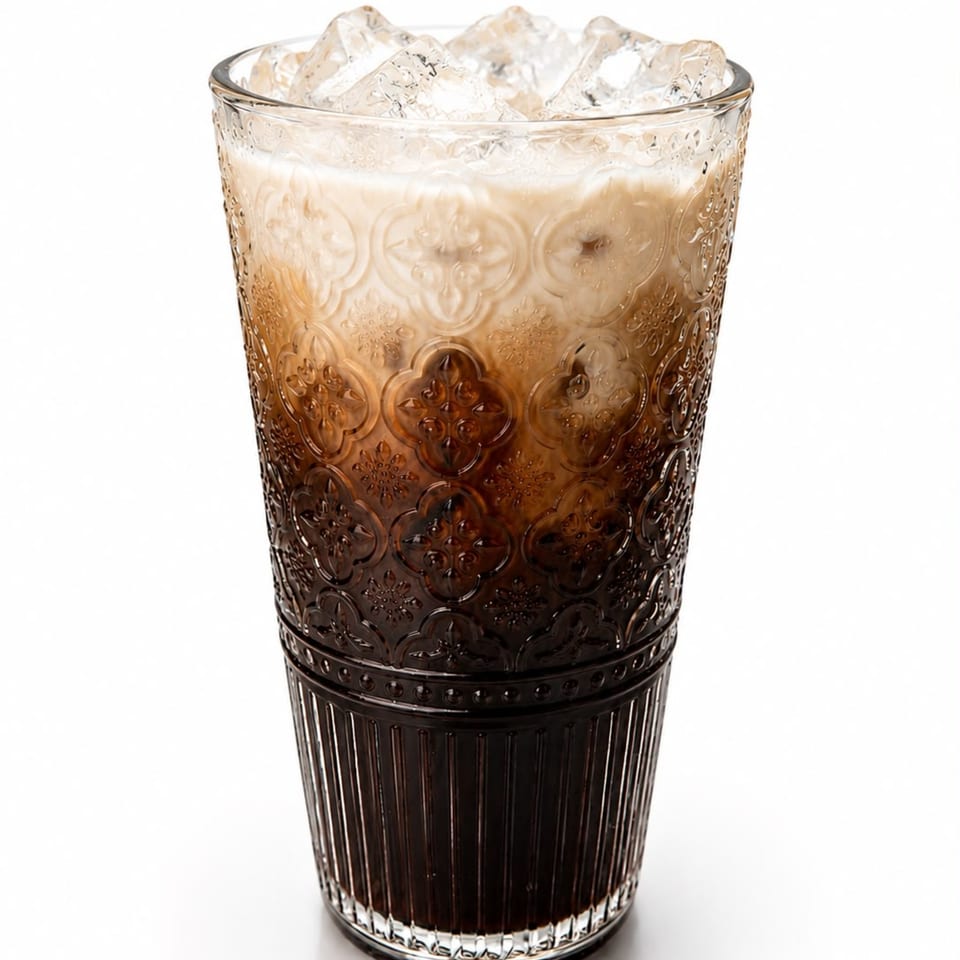 Iced coffee with milk in a tall, ornate glass, topped with ice cubes.