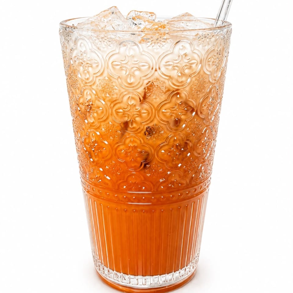 Iced Thai tea in an ornate glass with a straw, against a white background.
