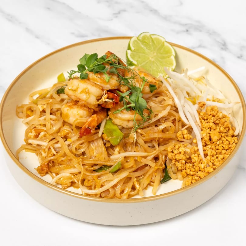 A plate of Jai Dee Restaurant's Pad Thai with shrimp, bean sprouts, crushed peanuts, and a lime wedge.