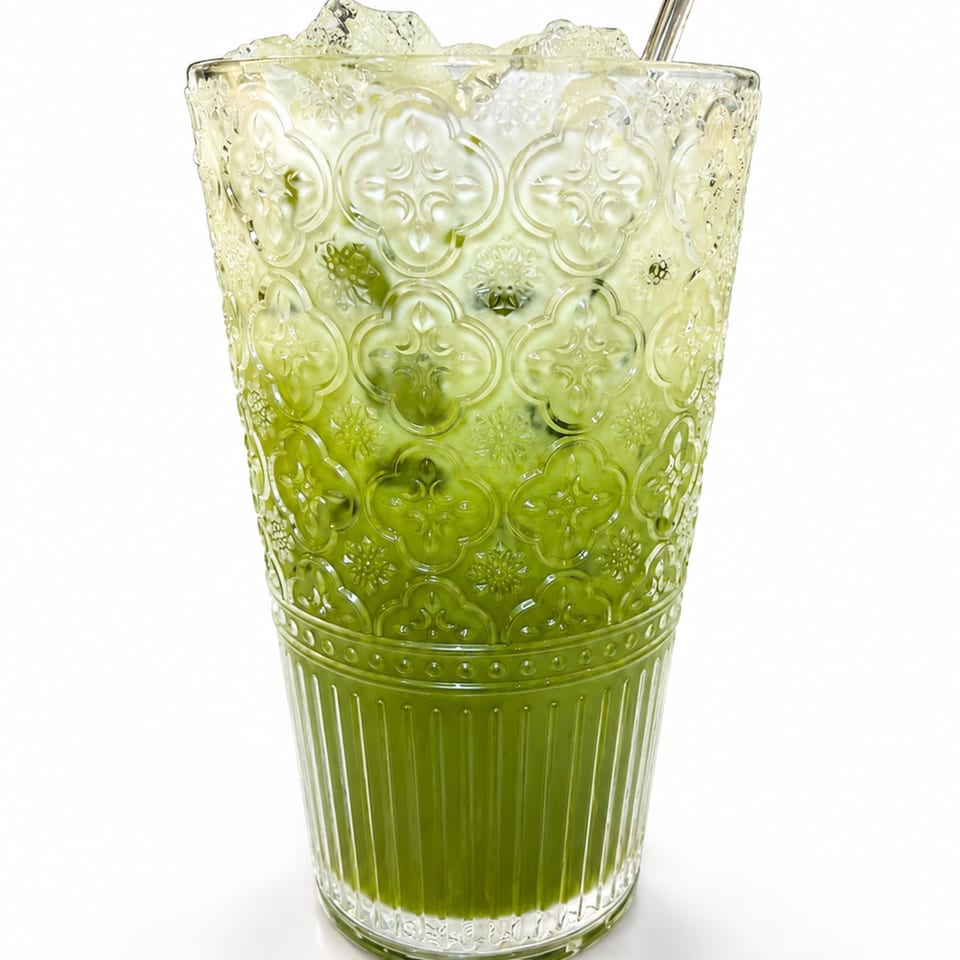Iced matcha latte in a decorative glass with a metal straw on a white background.