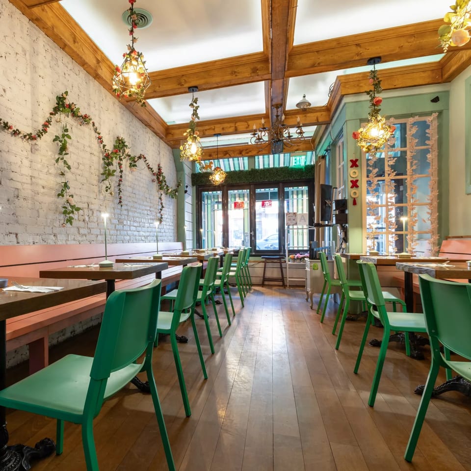 Interior of Jai Dee Restaurant with green chairs, wooden tables, white brick walls, and floral decor.