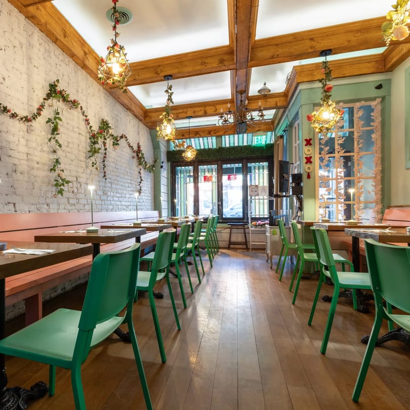 Interior of Jai Dee Restaurant with green chairs, wooden tables, white brick walls, and floral decor.